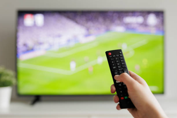 Close up of hand with remote controller and tv with football on background